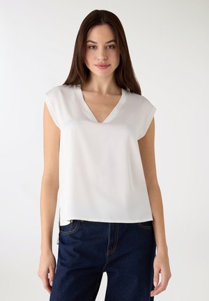 Blusa bianca a maniche corte con scollo a V, realizzata in tessuto liscio. Presenta spacchi laterali e una vestibilità rilassata, abbinata a jeans scuri.
