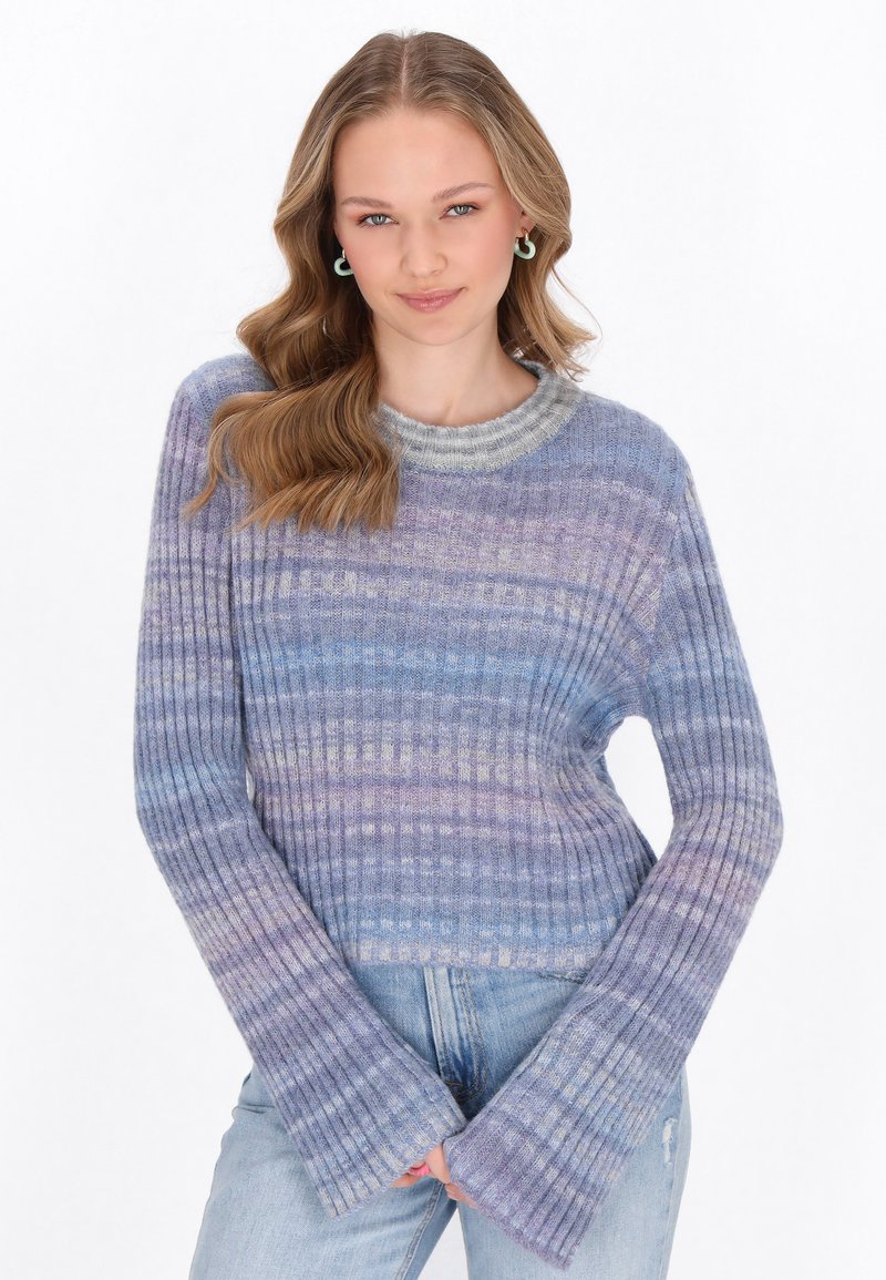 Maglione a righe viola e blu con un ampio colletto grigio e maniche svasate, abbinato a jeans azzurri chiari.