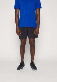 Blaues kurzärmliges Sportshirt, schwarze sportliche Shorts und schwarze Laufschuhe, alles für aktive Bekleidung konzipiert, mit minimalem Design und Farbkontrast.