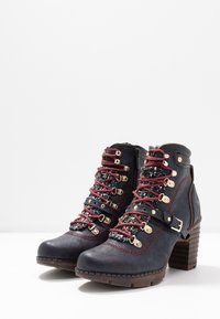 Par de botines de cuero azul oscuro con cordones rojos, ojales dorados, correa con hebilla, lengüeta de tela con patrones y tacones apilados.
