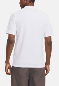 Polo shirt blanc avec un tissu texturé, des manches courtes et un col classique. Présente un ourlet droit et des fentes sur les côtés pour faciliter le mouvement.