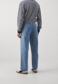 Ljusblå denimjeans med en avslappnad passform, med en midja i normalhöjd och subtila sömmar. Bärs med en svart och vit randig skjorta samt avslappnade skor.