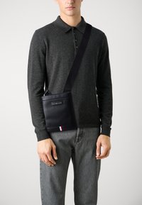 Borsa a tracolla in pelle blu navy con superficie testurizzata, dotata di una patch con il logo e di un accento a strisce in rosso, bianco e blu nella parte inferiore.