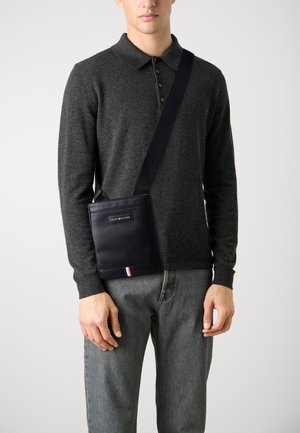 Borsa a tracolla in pelle blu navy con superficie testurizzata, dotata di una patch con il logo e di un accento a strisce in rosso, bianco e blu nella parte inferiore.