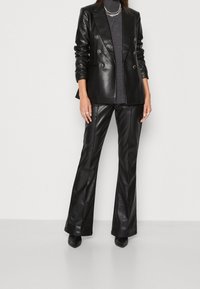 Blazer noir en cuir à double boutonnage avec des boutons métalliques, associé à un col roulé en maille gris foncé et un pantalon évasé en cuir noir.