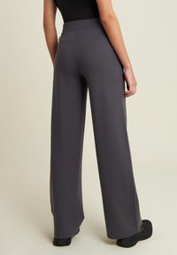 Pantalones de pierna ancha en tela gris, con una cinturilla elástica y una textura suave. El dobladillo cae alrededor de los tobillos. Se ven calzado negro.