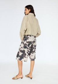 Giacca cropped beige chiaro e pantaloni corti lunghezza polpaccio con stampa a macchie di mucca nera e beige. L'outfit presenta una vestibilità rilassata e semplici sandali tipo slide.