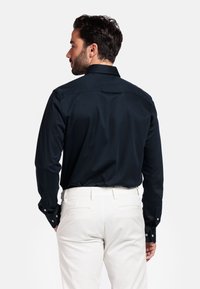 Marineblauw overhemd met lange mouwen, een gespreide kraag en knoopmanchetten, gecombineerd met lichtgekleurde broeken. Zachte textuur, op maat gemaakt ontwerp.