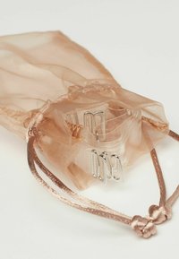 Pytlíček v růžově zlaté barvě vyrobený z průhledné tkaniny, obsahující plastové sponky a stříbrné papírové sponky. Pytlíček má zavírání na šňůrku.