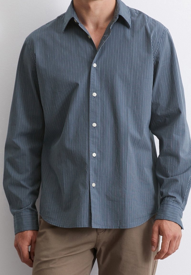 Camicia a righe in blu scuro e bianco, realizzata in tessuto leggero; presenta un colletto a punta e maniche lunghe con polsini bottonati.