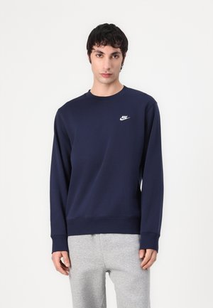 Marineblauwe Nike-sweater met een ronde hals, lange mouwen en logo op de linkerkant van de borst; gecombineerd met lichtgrijze sweatpants.