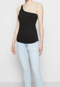 Czarny prążkowany top na jedno ramię, dopasowany krój, gładka tekstura. Połączony z jasnoniebieskimi skinny jeansami. Prosta, minimalistyczna estetyka.