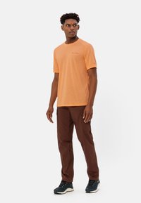 Camicetta arancione a maniche corte con scollatura rotonda, abbinata a pantaloni cargo marroni e scarpe blu scuro con suole bianche. Logo del marchio visibile in modo sottile.