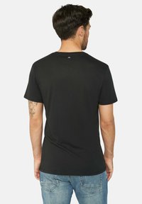 Černé tričko s krátkým rukávem a kulatým výstřihem, vyrobené z jemného materiálu. Na zadním výstřihu se nachází decentní modré logo. Nosit s modrými džíny.