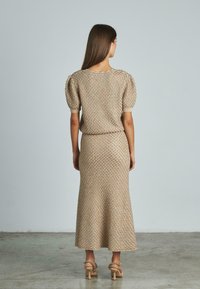 Abito a due pezzi in maglia beige con motivo testurizzato; maniche a sbuffo corte, gonna svasata di lunghezza media, abbinato a tacchi alti embelliti.