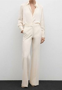 Blouse en soie crème avec une coupe décontractée et une patte de boutonnage, associée à un pantalon crème taille haute avec une coupe large et ajustée.