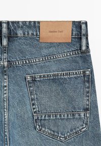 Achterkant van een blauwe spijkerbroek met één zak, voorzien van stiksel en een bruin leren label met de tekst "Massimo Dutti" op de tailleband.