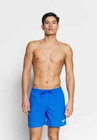 Shorts de bain bleus en tissu léger, dotés d'une taille élastique, d'un cordon de serrage et d'un logo blanc sur le bas à gauche.