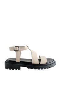 Sandale bej din piele cu barete încrucișate și cataramă reglabilă la gleznă. Talpa neagră din cauciuc are un model aspru pentru aderență.