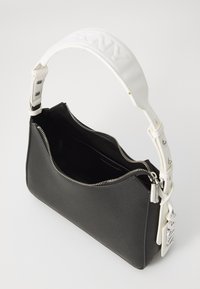 Borsa a tracolla in pelle nera con finitura testurizzata, forma curva, zip argentata e tracolla bianca con lettering impresso. Interno aperto visibile.