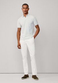 Svetle šedé polo tričko s krátkým rukávem, spárované s bílými kalhotami a tmavohnědými slip-on botami. Hladké látky a přiléhavý střih.