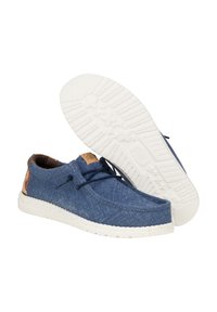 Scarpe in tessuto blu con una consistenza morbida, dotate di una suola in gomma bianca, dettagli marroni sul tallone e lacci neri. Design wingtip.