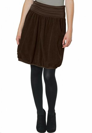 Brown corduroy skirt with a gathered design, wide waistband, and side pockets. Worn over black tights and heeled boots.