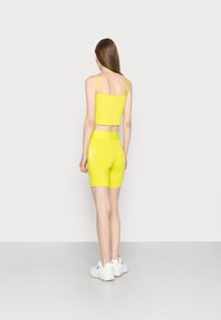 Světlě žlutý ribbený crop top s tenkými ramínky, doplněný o odpovídající cyklistické šortky se bílým logem na boku. Bílé tenisky.