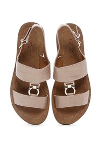 Beige faux leather sandals with cross straps, metallic buckle accents, and a molded cork footbed. Textured surface with a smooth finish.