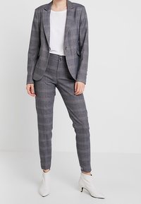 Grå rutigt kavaj och matchande byxor, tillverkad av texturerat tyg. Kombinerad med en vit topp och ankelstövlar. Vila design, slank silhuett.