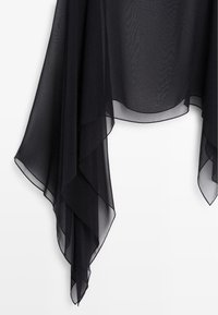 Sort gennemsigtigt stof med lagdelt, asymmetrisk spids kant mod en ensfarvet hvid baggrund.