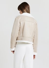 Giacca in finta suede beige con colletto e polsini in shearling bianco, design cropped, cuciture visibili e una texture liscia.
