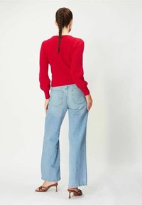 Röd stickad tröja med puffärmar, kombinerad med ljusblå vida jeans och bruna klacksandaler, sedd bakifrån.