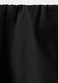 Černý závěs s nabráním na horním okraji zavěšený na jednobarevném světle pozadí.