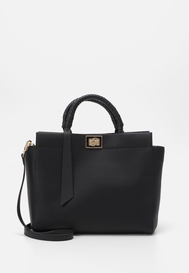 Sac à main texturé noir avec poignées courtes enveloppées, fermoir rectangulaire doré, longue bandoulière, et un ruban noir décoratif sur fond blanc.