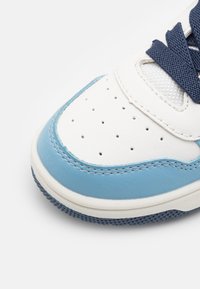 Tossut, joissa on valkoinen nahka-osa vaaleansinisin yksityiskohdin ja rei'ityksin, laivaston siniset nauhat ja teksturoitu kumipohja.