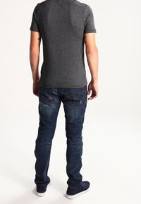 Grårandig kortärmad skjorta i kombination med mörkblå jeans. Har en smal passform och synlig sömnad på bakfickorna.