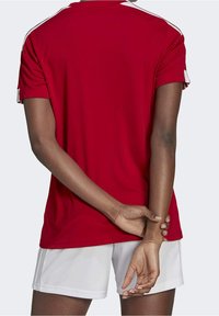 Czerwona sportowa koszulka z krótkimi rękawami, z białymi akcentami na ramionach. W zestawie z białymi spodenkami o gładkiej fakturze.
