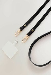 Correas de cuero negro texturizado con herrajes dorados, clips y cierres; incluye una etiqueta blanca con un anillo metálico.