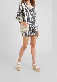 Svartvit mönstrad skjorta med knappar och matchande shorts. Vita plattformssandaler och en liten krämfärgad crossbody-väska.