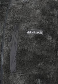 Giacca in pile nera con zip frontale, tessuto testurizzato e tasca sul petto con logo Columbia. Materiale morbido e peloso.