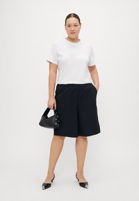 White short-sleeve shirt, black knee-length shorts, black bag with eyelet details, and black pointed-toe shoes. Simple and casual outfit.