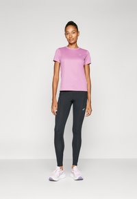Roze sport T-shirt, aansluitend ontwerp, gecombineerd met zwarte leggings. Witte en lavendel hardloopschoenen maken de look compleet. Eenvoudig logo detail zichtbaar.