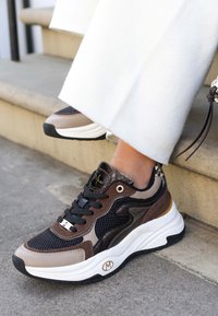 Hnědé a černé tenisky s mřížkovaným a umělou kůží, texturovanými detaily, bílou podrážkou a zlatými prvky.