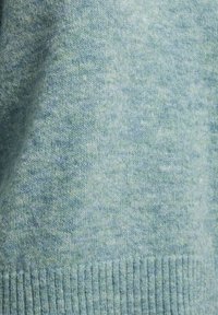 Tessuto lavorato a maglia azzurro chiaro con una consistenza morbida, caratterizzato da un delicato motivo mélange. Il bordo inferiore presenta un dettaglio a coste.