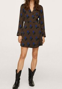 Vestido marrón de estilo envolvente con mangas largas, que presenta patrones florales azules. Se lleva con botas de cowboy negras. Textura suave, diseño hasta la rodilla.