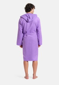 Accappatoio con cappuccio in lilla chiaro, realizzato in tessuto morbido, con maniche lunghe, cintura da annodare e lunghezza al ginocchio. Presenta un cappuccio testurizzato.