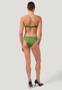 Bikini deux pièces vert avec un haut à bretelles derrière et un bas à découpe haute. Texture lisse avec une légère brillance. Associé à des escarpins noirs.