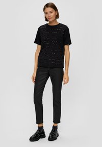 Czarny t-shirt z poziomymi prążkami teksturowymi, w połączeniu z czarnymi spodniami slim-fit. Buty są czarne, o połyskującym wykończeniu i grubych podeszwach.