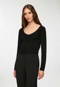 Czarny sweter dzianinowy z dekoltem w kształcie V i ściągaczami na rękawach. Dopasowany krój, materiał o fakturze, zestawiony z czarnymi spodniami w kant.